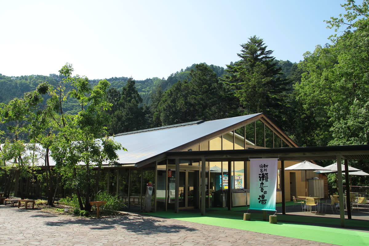 秋川渓谷リゾート 瀬音の湯の入口——木造の建物と緑（東京都あきる野市乙津）
